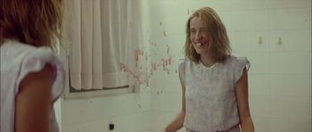 Movie still from “Dogtooth” (2009), directed by Yorgos Lanthimos – A woman in a white dress standing next to a white wall; Medium shot, Over the shoulder angle