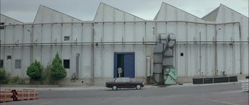 Movie still from “Dogtooth” (2009), directed by Yorgos Lanthimos – A car parked on the side of the road next to a building; Extreme Wide shot, Low angle