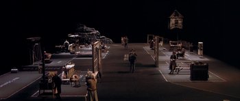 Movie still from “Dogville” (2003), directed by Lars von Trier – A group of people standing in an empty parking lot at night; Extreme Wide shot, High angle