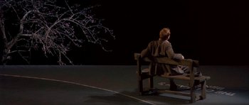 Movie still from “Dogville” (2003), directed by Lars von Trier – A man sitting on a bench in front of a tree; Wide shot, High angle