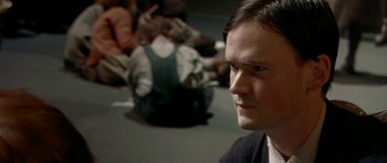 Movie still from “Dogville” (2003), directed by Lars von Trier – A man sitting on the ground in front of a group of people; Close Up shot, High angle