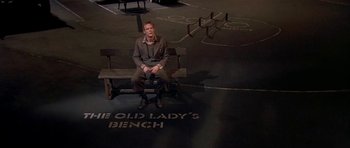 Movie still from “Dogville” (2003), directed by Lars von Trier – A man sitting on top of a wooden bench; Wide shot, High angle