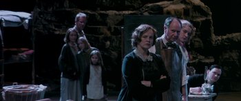 Movie still from “Dogville” (2003), directed by Lars von Trier – A group of people standing in a dark room; Medium shot, High angle