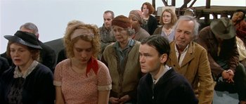Movie still from “Dogville” (2003), directed by Lars von Trier – A group of people standing around each other in a room; Medium shot, High angle