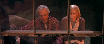 Movie still from “Dogville” (2003), directed by Lars von Trier – An older man and a younger woman looking out of a window; Medium shot, High angle