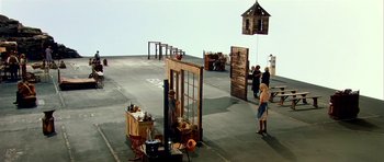 Movie still from “Dogville” (2003), directed by Lars von Trier – A group of people standing around a wooden structure; Extreme Wide shot, High angle