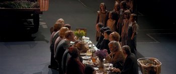 Movie still from “Dogville” (2003), directed by Lars von Trier – A group of people sitting at a table with plates of food; Wide shot, High angle