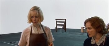 Movie still from “Dogville” (2003), directed by Lars von Trier – A woman standing in front of a wooden bench; Medium shot, High angle