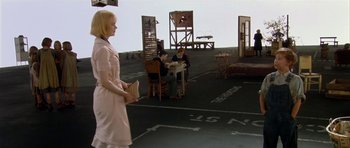 Movie still from “Dogville” (2003), directed by Lars von Trier – Two people sitting at a table in an empty parking lot; Wide shot, High angle
