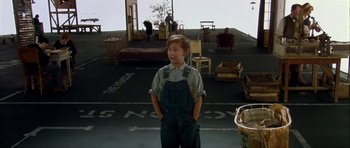 Movie still from “Dogville” (2003), directed by Lars von Trier – A young boy standing in a parking lot with his hands in his pockets; Wide shot, High angle