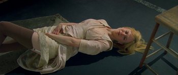 Movie still from “Dogville” (2003), directed by Lars von Trier – A woman laying on the ground with her hands on her stomach; Medium shot, Overhead angle