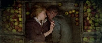Movie still from “Dogville” (2003), directed by Lars von Trier – A man and a woman embracing each other in front of apples; Medium shot, Overhead angle