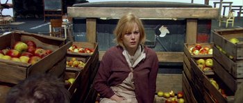Movie still from “Dogville” (2003), directed by Lars von Trier – A woman sitting in front of crates filled with apples; Medium shot, High angle