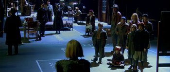 Movie still from “Dogville” (2003), directed by Lars von Trier – A group of people standing on the floor of a room; Wide shot, High angle