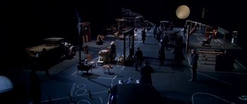 Movie still from “Dogville” (2003), directed by Lars von Trier – An aerial view of a stage with people in the background; Extreme Wide shot, High angle