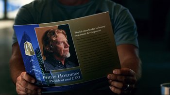 Movie still from “Dolphin Tale” (2011), directed by Charles Martin Smith – A person holding a book with a picture of a man on it; Close Up shot, High angle