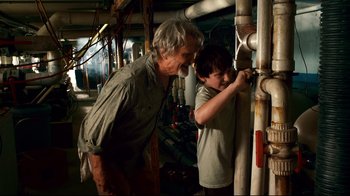 Movie still from “Dolphin Tale” (2011), directed by Charles Martin Smith – A man and a boy working on pipes in a room; Medium shot, Over the shoulder angle