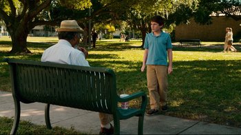 Movie still from “Dolphin Tale” (2011), directed by Charles Martin Smith – A man sitting on top of a green park bench next to a boy; Wide shot, Over the shoulder angle