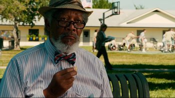 Movie still from “Dolphin Tale” (2011), directed by Charles Martin Smith – An older man wearing a hat and a bow tie while sitting on a park bench; Close Up shot, Over the shoulder angle