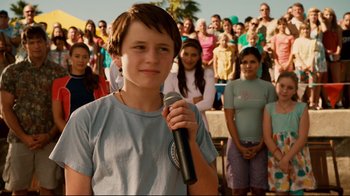 Movie still from “Dolphin Tale” (2011), directed by Charles Martin Smith – A young boy holding a microphone in front of a crowd; Medium shot, Over the shoulder angle