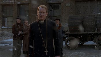 Movie still from “Dominion: Prequel to the Exorcist” (2005), directed by Paul Schrader – A man wearing a priest's outfit standing in front of other men; Medium shot, Over the shoulder angle