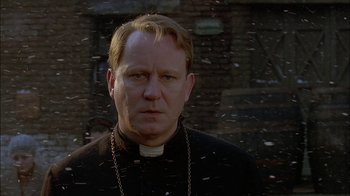 Movie still from “Dominion: Prequel to the Exorcist” (2005), directed by Paul Schrader – A man wearing a priest's outfit standing in front of a brick building; Close Up shot, Over the shoulder angle