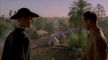 Movie still from “Dominion: Prequel to the Exorcist” (2005), directed by Paul Schrader – Two men are standing in front of tents in the desert; Medium shot, Over the shoulder angle