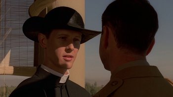 Movie still from “Dominion: Prequel to the Exorcist” (2005), directed by Paul Schrader – A man wearing a priest's outfit and a black hat talking to a man in uniform; Close Up shot, Over the shoulder angle