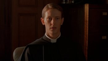 Movie still from “Dominion: Prequel to the Exorcist” (2005), directed by Paul Schrader – A man wearing a priest's outfit in front of a wall; Close Up shot, Low angle