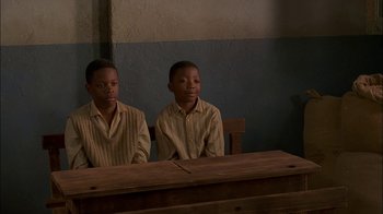 Movie still from “Dominion: Prequel to the Exorcist” (2005), directed by Paul Schrader – Two young boys sitting in front of a wooden table; Medium shot, High angle