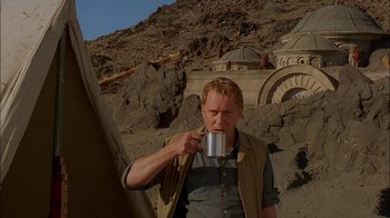 Movie still from “Dominion: Prequel to the Exorcist” (2005), directed by Paul Schrader – A man is drinking from a mug outside; Medium shot, Low angle