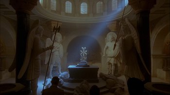 Movie still from “Dominion: Prequel to the Exorcist” (2005), directed by Paul Schrader – A group of people sitting in a room with statues; Extreme Wide shot, High angle