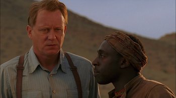 Movie still from “Dominion: Prequel to the Exorcist” (2005), directed by Paul Schrader – A man standing next to another man on a hill; Close Up shot, Over the shoulder angle