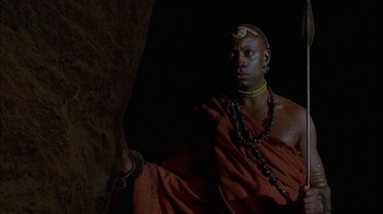 Movie still from “Dominion: Prequel to the Exorcist” (2005), directed by Paul Schrader – A man in a red robe sitting in front of a rock wall; Medium shot, Low angle