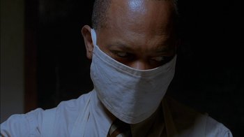 Movie still from “Dominion: Prequel to the Exorcist” (2005), directed by Paul Schrader – A man wearing a face mask and a tie; Close Up shot, Low angle