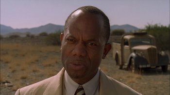 Movie still from “Dominion: Prequel to the Exorcist” (2005), directed by Paul Schrader – A man in a suit and tie standing in front of an old truck; Close Up shot, Low angle