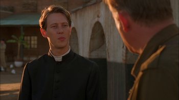 Movie still from “Dominion: Prequel to the Exorcist” (2005), directed by Paul Schrader – A man wearing a priest's outfit talking to another man in front of a building; Close Up shot, Over the shoulder angle