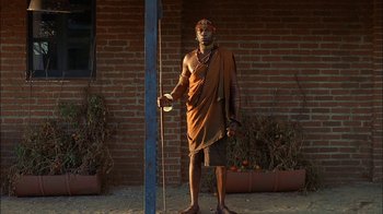 Movie still from “Dominion: Prequel to the Exorcist” (2005), directed by Paul Schrader – A man standing in front of a brick building holding a pole; Wide shot, Low angle