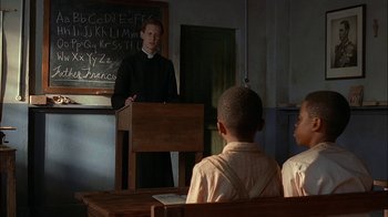 Movie still from “Dominion: Prequel to the Exorcist” (2005), directed by Paul Schrader – A man is giving a lecture to a group of children; Medium shot, Over the shoulder angle