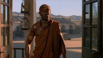 Movie still from “Dominion: Prequel to the Exorcist” (2005), directed by Paul Schrader – A man in a brown robe standing on a dirt road; Medium shot, Low angle