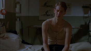 Movie still from “Dominion: Prequel to the Exorcist” (2005), directed by Paul Schrader – A man sitting on a bed in a room; Close Up shot, Low angle