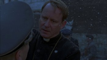 Movie still from “Dominion: Prequel to the Exorcist” (2005), directed by Paul Schrader – A man wearing a priest's outfit and a chain around his neck; Close Up shot, Over the shoulder angle