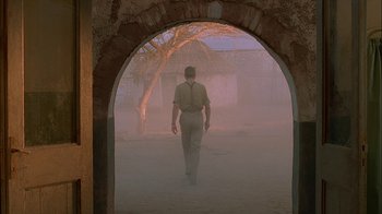Movie still from “Dominion: Prequel to the Exorcist” (2005), directed by Paul Schrader – A man walking through an archway on a foggy day; Wide shot, Low angle