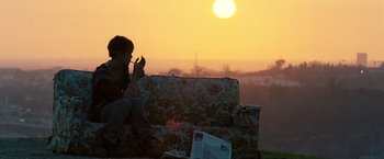 Movie still from “Domino” (2005), directed by Tony Scott – A person sitting on a couch in front of a sunset; Wide shot, Over the shoulder angle