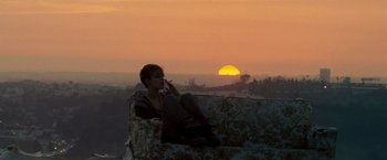 Movie still from “Domino” (2005), directed by Tony Scott – A woman sitting on top of a couch talking on a phone; Wide shot, Low angle