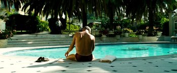 Movie still from “Domino” (2005), directed by Tony Scott – A man sitting on the side of a swimming pool; Wide shot, Low angle