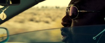 Movie still from “Domino” (2005), directed by Tony Scott – A man driving a car with his sunglasses on his face; Close Up shot, Low angle