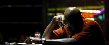Movie still from “Domino” (2005), directed by Tony Scott – A man sitting at a table with a glass of water; Close Up shot, High angle