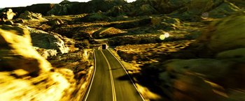 Movie still from “Domino” (2005), directed by Tony Scott – A car driving down a road in the middle of the desert; Extreme Wide shot, High angle