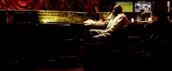 Movie still from “Domino” (2005), directed by Tony Scott – A man sitting at a table in front of a bar; Wide shot, Low angle